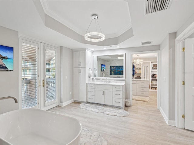 bathroom featuring a chandelier, ornamental molding, a tub to relax in, and a raised ceiling