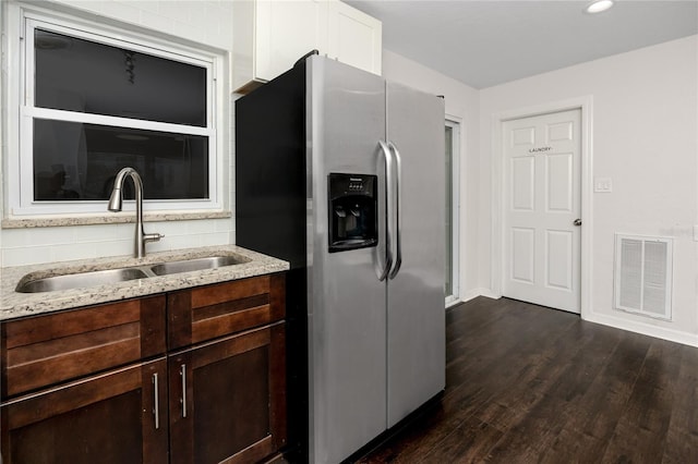 kitchen with light stone countertops, dark brown cabinetry, stainless steel refrigerator with ice dispenser, dark wood-type flooring, and sink