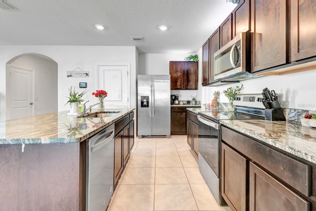 kitchen featuring light tile patterned floors, a center island with sink, stainless steel appliances, a textured ceiling, and sink