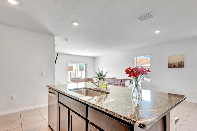 kitchen featuring light tile patterned floors, an island with sink, dishwasher, light stone countertops, and sink