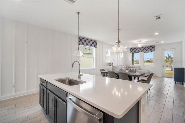 kitchen featuring pendant lighting, sink, dishwasher, light stone counters, and an island with sink