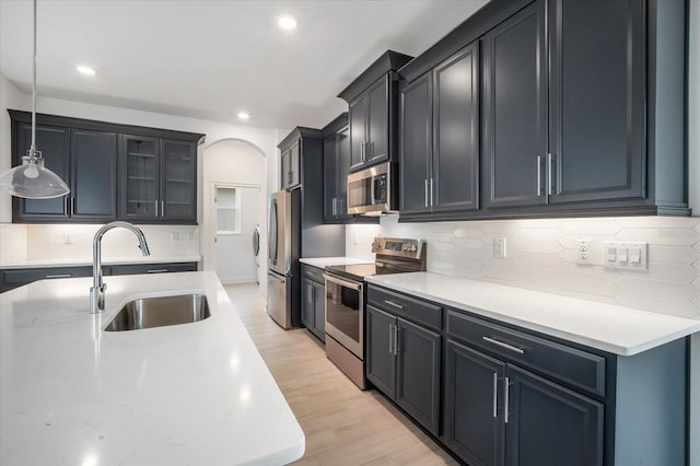 kitchen featuring sink, hanging light fixtures, light wood-type flooring, appliances with stainless steel finishes, and backsplash