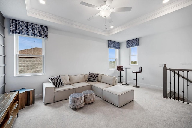 living room featuring ceiling fan, ornamental molding, a tray ceiling, and light carpet