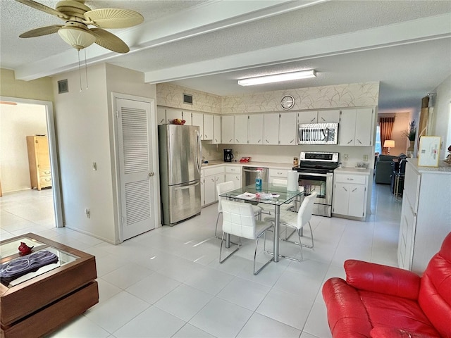 kitchen featuring white cabinets, appliances with stainless steel finishes, beamed ceiling, light tile patterned flooring, and ceiling fan