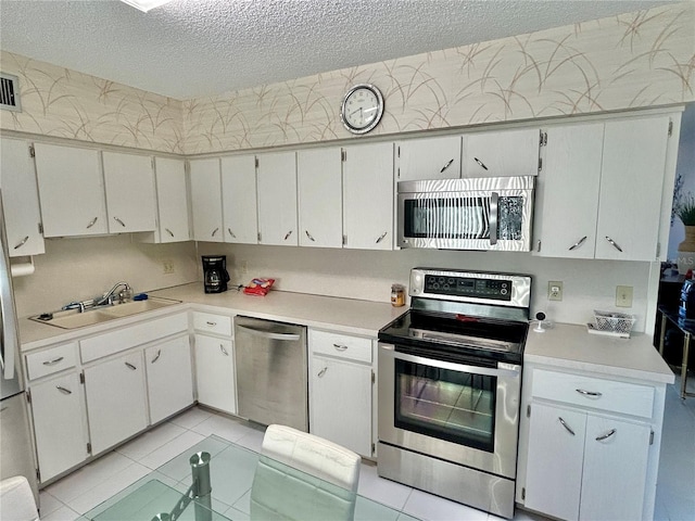 kitchen featuring a textured ceiling, appliances with stainless steel finishes, white cabinets, and sink