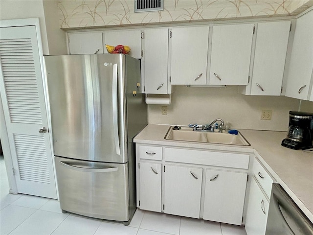 kitchen featuring dishwashing machine, sink, stainless steel refrigerator, light tile patterned floors, and white cabinets