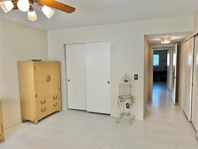 bedroom with ceiling fan, a textured ceiling, a closet, and light tile patterned flooring