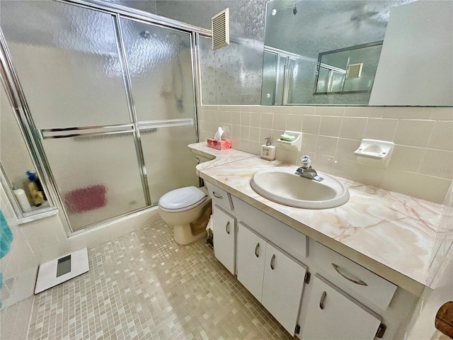 bathroom with toilet, a shower with shower door, tile patterned flooring, tile walls, and vanity