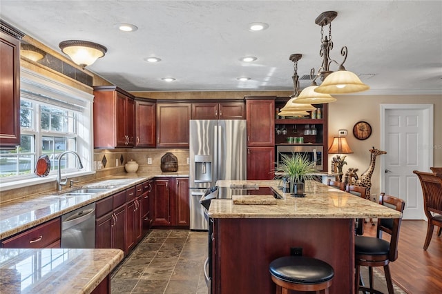 kitchen featuring appliances with stainless steel finishes, a kitchen island, sink, hanging light fixtures, and a kitchen breakfast bar