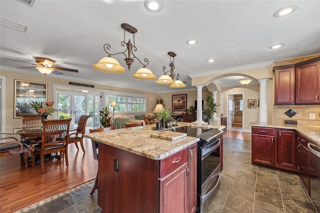 kitchen with appliances with stainless steel finishes, decorative light fixtures, a kitchen island, decorative columns, and decorative backsplash