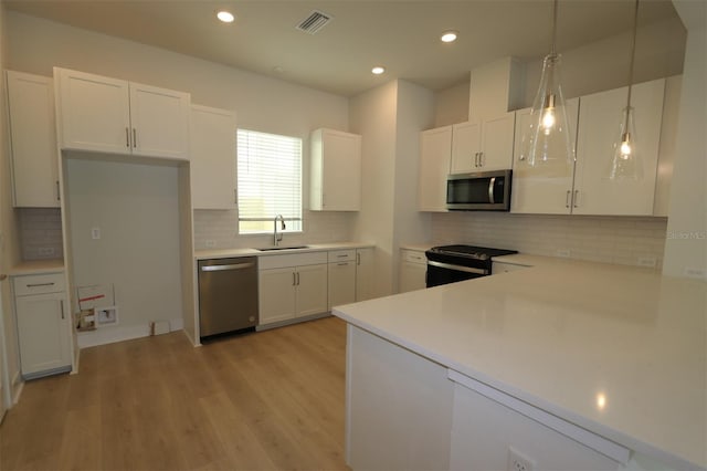 kitchen with pendant lighting, sink, white cabinetry, light hardwood / wood-style flooring, and appliances with stainless steel finishes