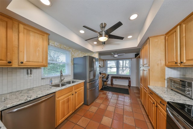 kitchen featuring appliances with stainless steel finishes, decorative backsplash, sink, ceiling fan, and a tray ceiling