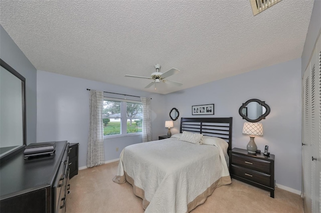 bedroom with a textured ceiling, ceiling fan, a closet, and light colored carpet