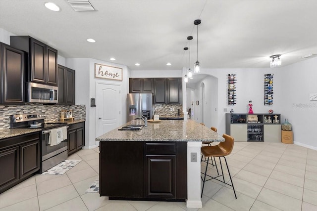 kitchen with a breakfast bar area, a center island with sink, appliances with stainless steel finishes, pendant lighting, and decorative backsplash