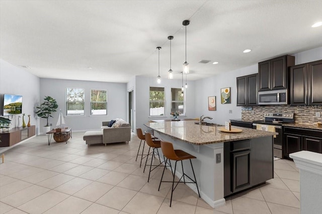 kitchen featuring appliances with stainless steel finishes, decorative light fixtures, tasteful backsplash, a kitchen bar, and a kitchen island with sink