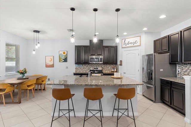 kitchen featuring hanging light fixtures, stainless steel appliances, tasteful backsplash, an island with sink, and a kitchen bar