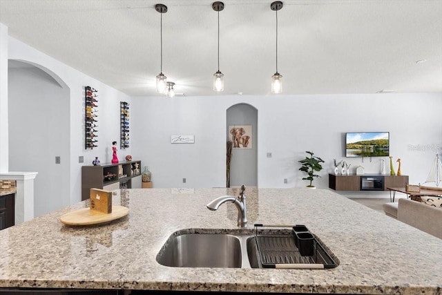 kitchen with sink, a center island with sink, light stone counters, and decorative light fixtures