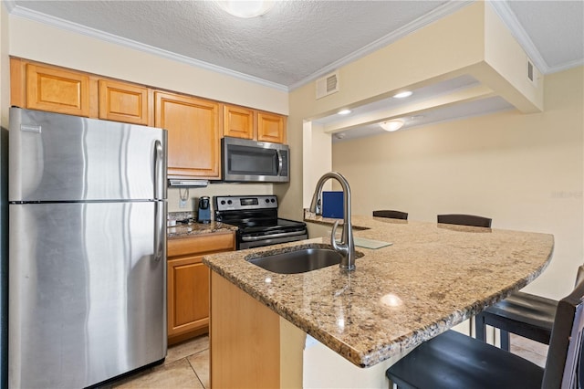 kitchen featuring a textured ceiling, stainless steel appliances, an island with sink, light stone counters, and a breakfast bar