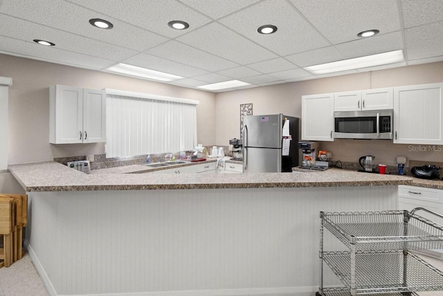 kitchen with appliances with stainless steel finishes, a paneled ceiling, sink, white cabinets, and kitchen peninsula