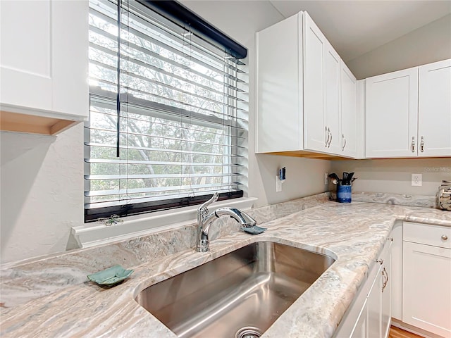 kitchen with light stone counters, sink, and white cabinetry