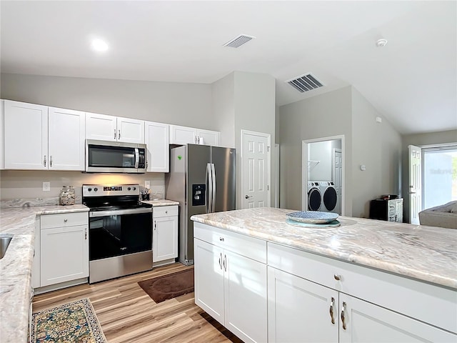 kitchen with appliances with stainless steel finishes, white cabinets, light stone countertops, washing machine and clothes dryer, and lofted ceiling