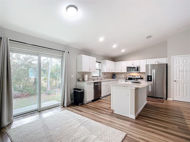 kitchen featuring a center island, light hardwood / wood-style floors, appliances with stainless steel finishes, white cabinetry, and lofted ceiling