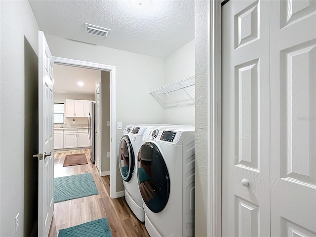 washroom with washer and dryer, light hardwood / wood-style floors, and a textured ceiling