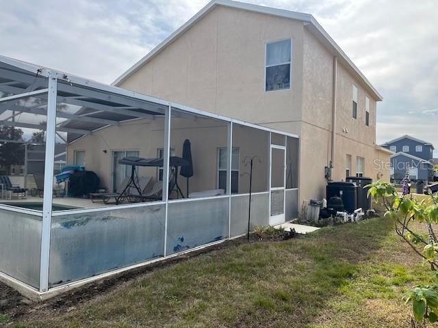 back of house featuring glass enclosure, central AC, a lawn, and a patio