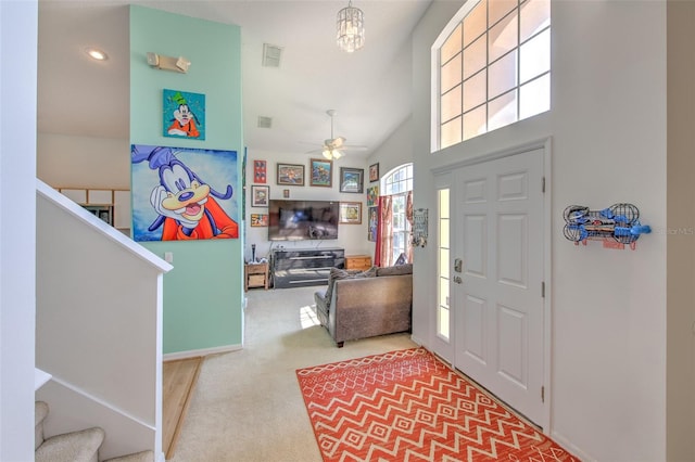 foyer entrance with a towering ceiling, carpet floors, and ceiling fan with notable chandelier