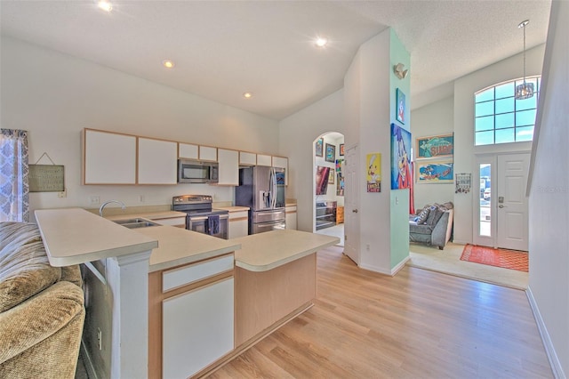 kitchen featuring high vaulted ceiling, sink, kitchen peninsula, stainless steel appliances, and light wood-type flooring