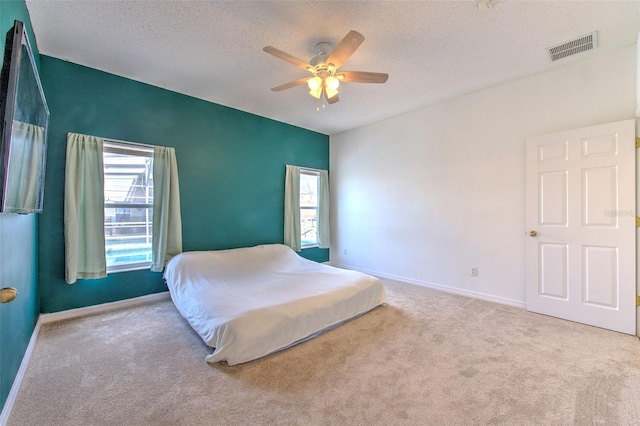 bedroom featuring ceiling fan, light colored carpet, and a textured ceiling