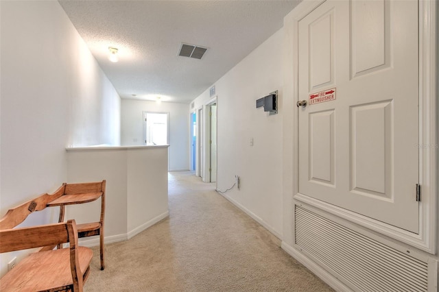 hallway featuring light carpet and a textured ceiling