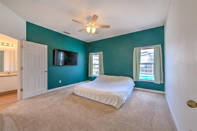 bedroom with multiple windows, ceiling fan, light colored carpet, and a textured ceiling