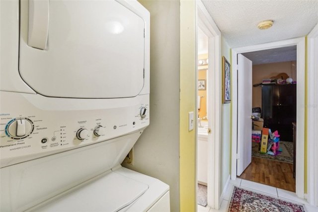 laundry area featuring stacked washing maching and dryer, light tile patterned floors, and a textured ceiling