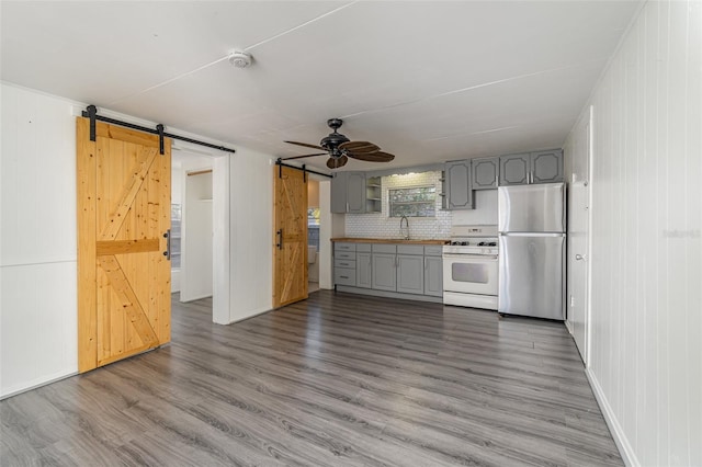 kitchen featuring sink, gray cabinetry, stainless steel fridge, white gas range, and a barn door