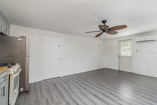 unfurnished living room featuring ceiling fan, a wall mounted AC, and light wood-type flooring