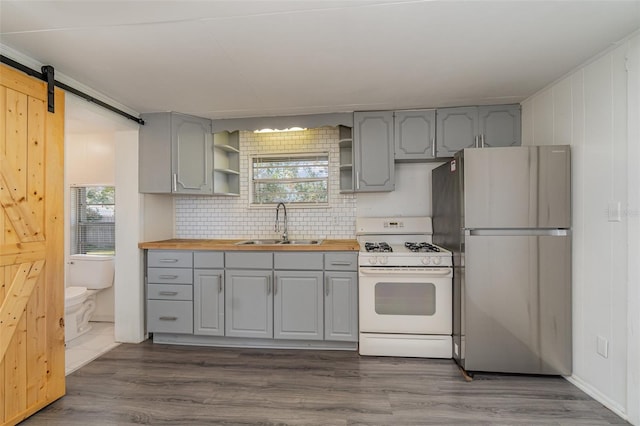 kitchen featuring wood counters, stainless steel refrigerator, sink, a barn door, and white gas stove