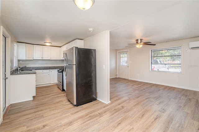 kitchen with appliances with stainless steel finishes, a wall mounted air conditioner, white cabinetry, sink, and light hardwood / wood-style floors