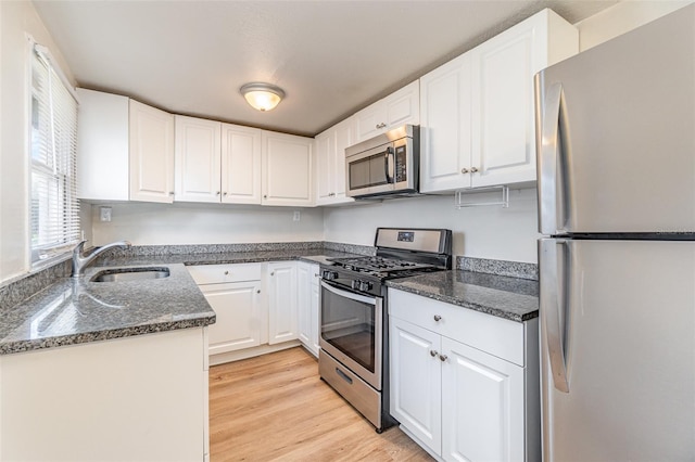 kitchen featuring white cabinetry, sink, dark stone countertops, stainless steel appliances, and light wood-type flooring