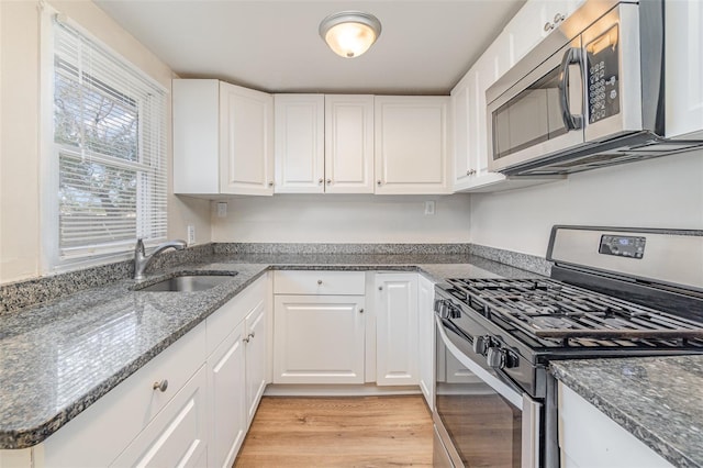 kitchen with white cabinetry, sink, dark stone countertops, stainless steel appliances, and light hardwood / wood-style flooring