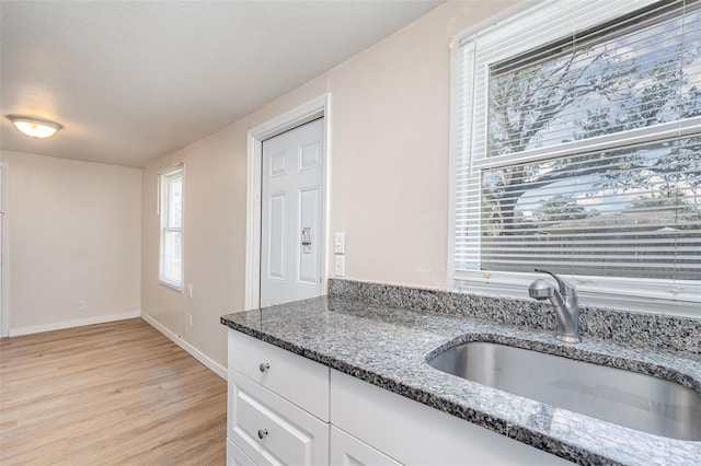 kitchen featuring white cabinetry, dark stone counters, sink, and light wood-type flooring