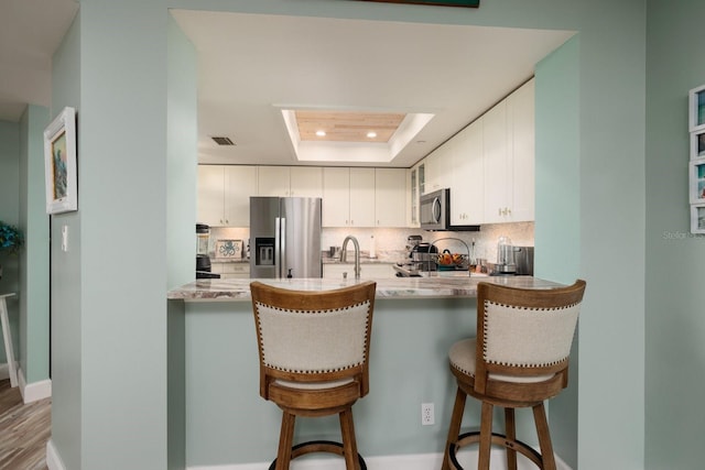 kitchen with white cabinetry, stainless steel appliances, backsplash, kitchen peninsula, and a tray ceiling