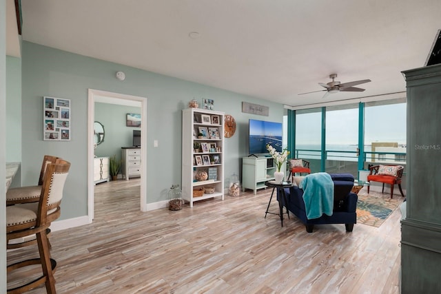 living room with ceiling fan, a wall of windows, and light hardwood / wood-style flooring