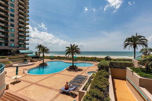 view of pool with a hot tub, a water view, and a patio