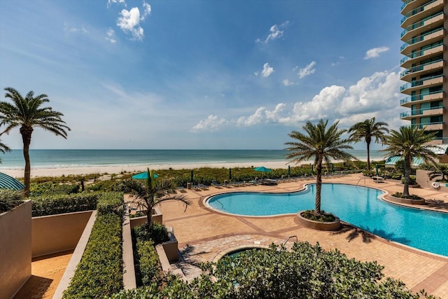 view of pool with a patio area, a water view, and a view of the beach