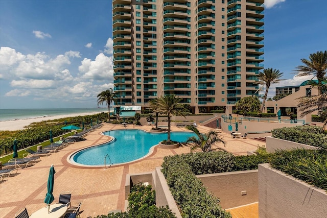 view of pool with a water view, a patio area, and a view of the beach