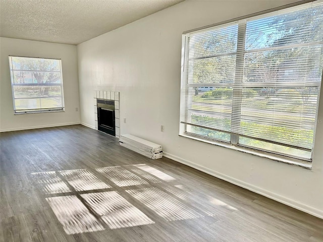 unfurnished living room featuring hardwood / wood-style flooring, a tiled fireplace, and a textured ceiling