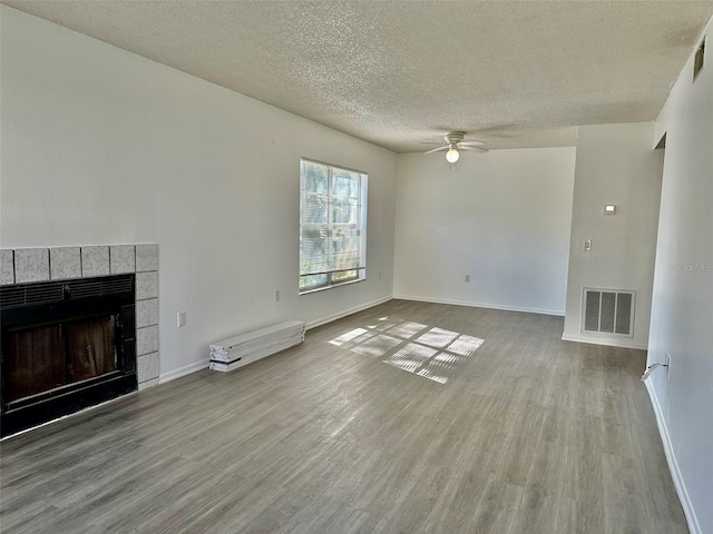 unfurnished living room featuring ceiling fan, a textured ceiling, a fireplace, and wood-type flooring