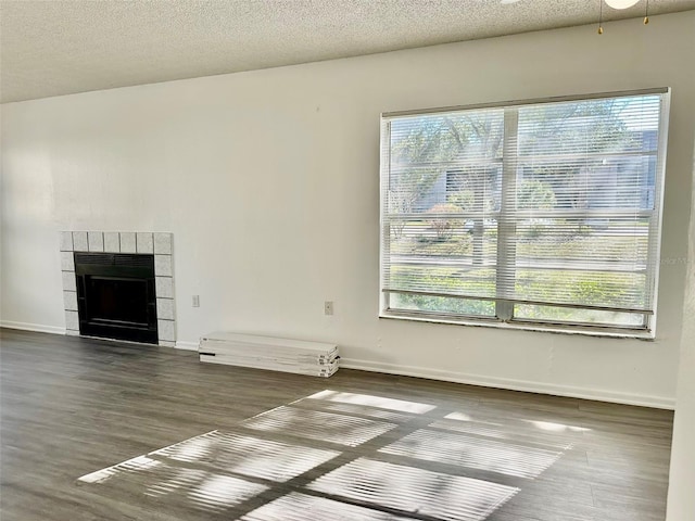 unfurnished living room featuring a textured ceiling, a tile fireplace, dark hardwood / wood-style floors, and a healthy amount of sunlight