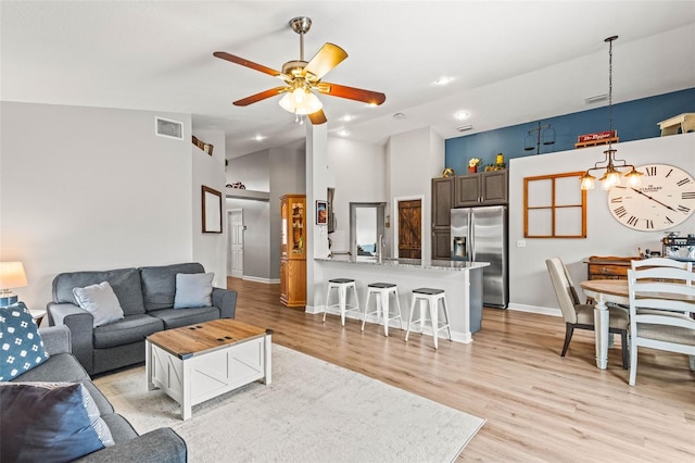 living room with high vaulted ceiling, ceiling fan with notable chandelier, and light hardwood / wood-style flooring